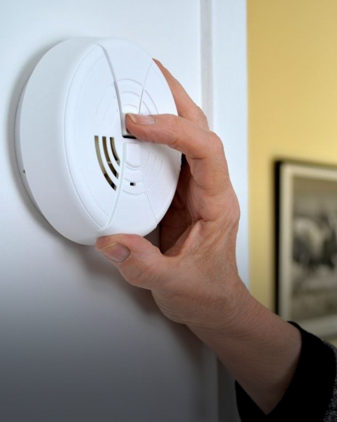 Hand plaatst een rookmelder aan het plafond van een woning